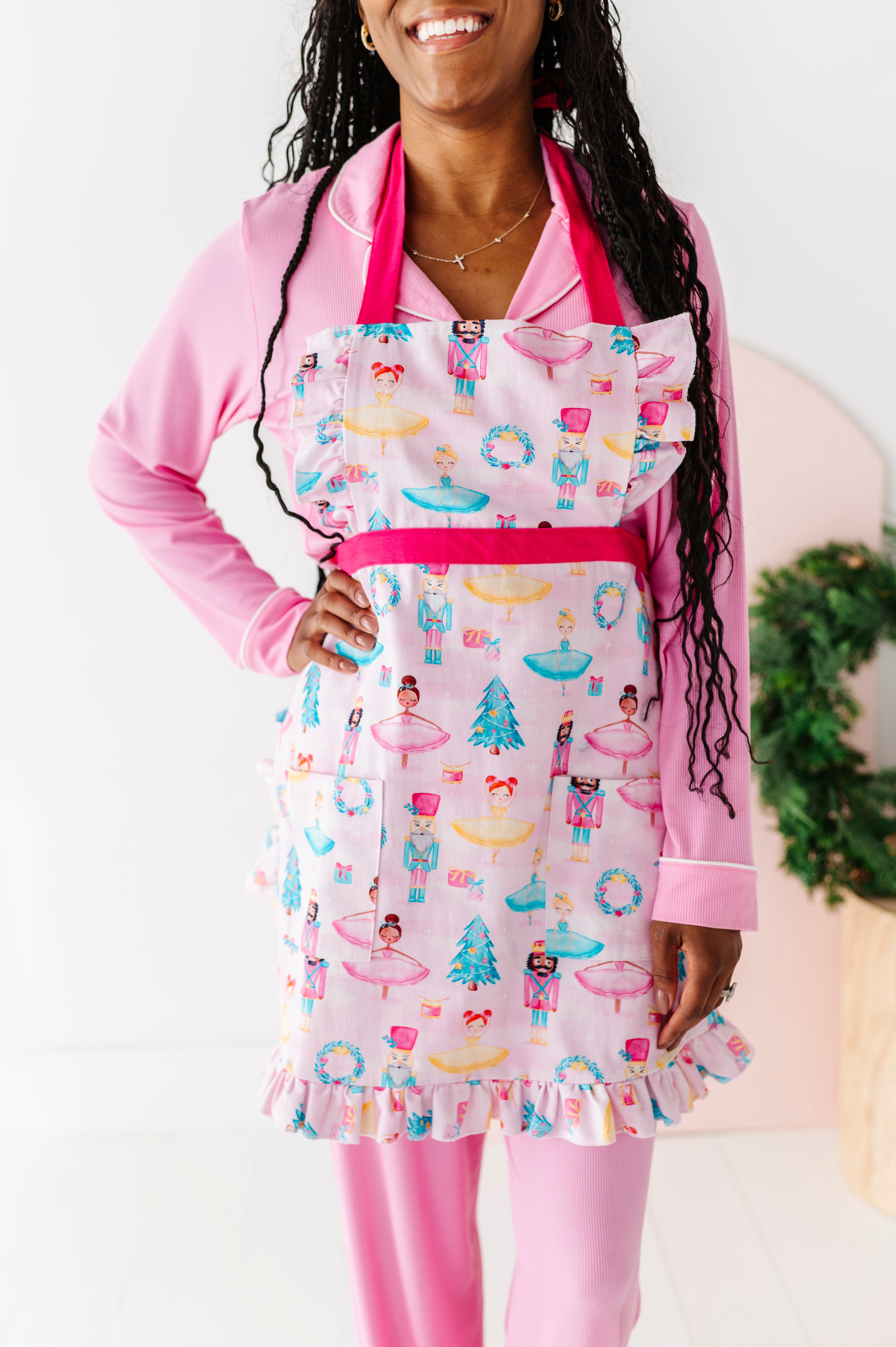 Woman wearing a light pink apron with a sugarplum fairy design, including ballerinas and nutcrackers